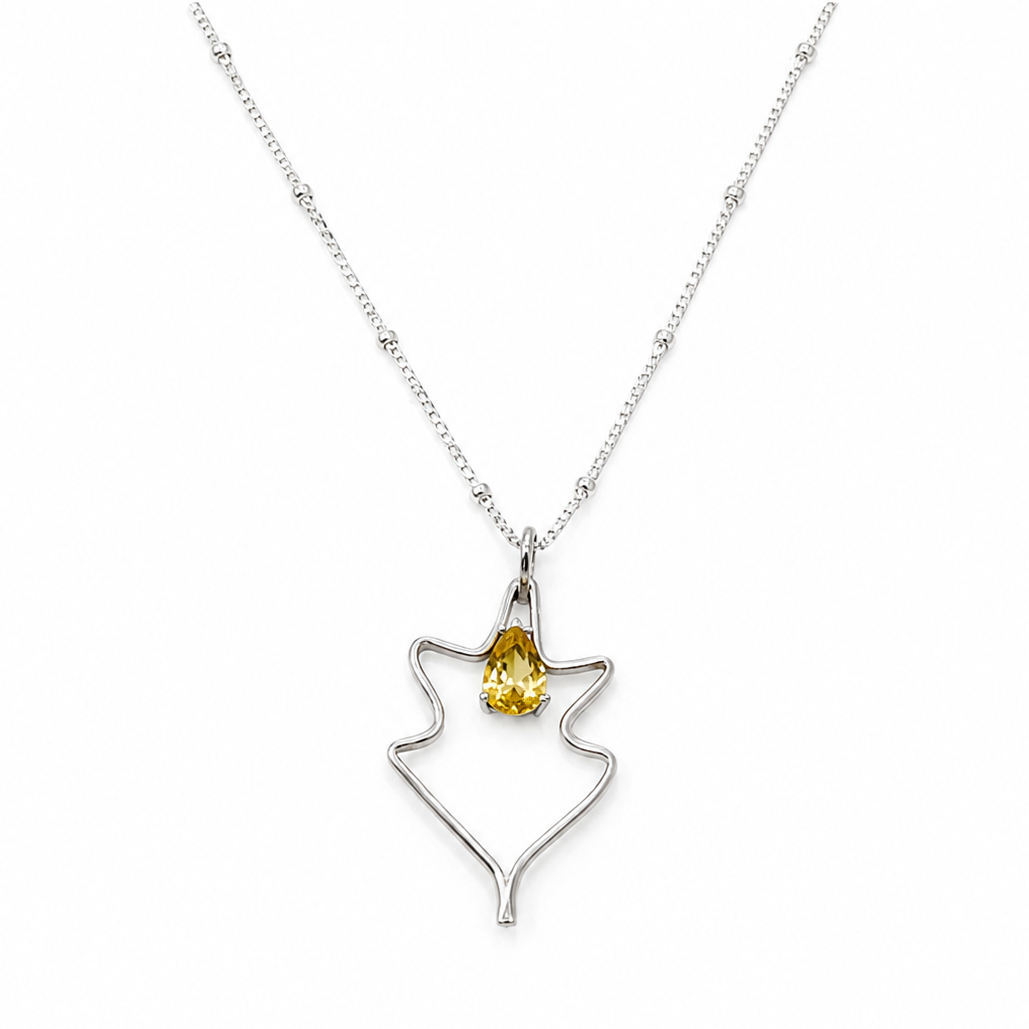 A silver necklace with minimal leaf-shaped pendant with a yellow gemstone at the center.
