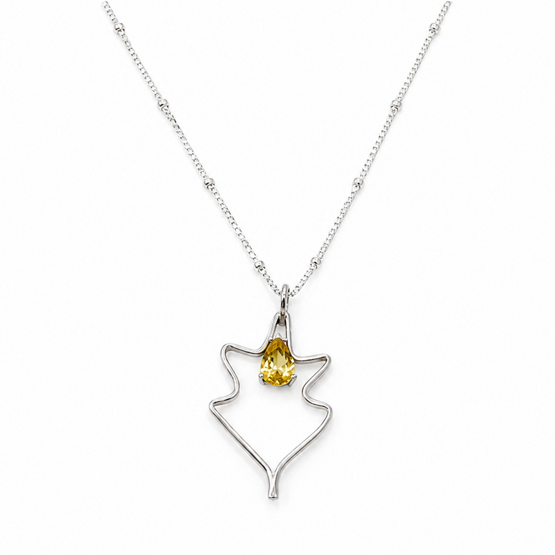 A silver necklace with minimal leaf-shaped pendant with a yellow gemstone at the center.