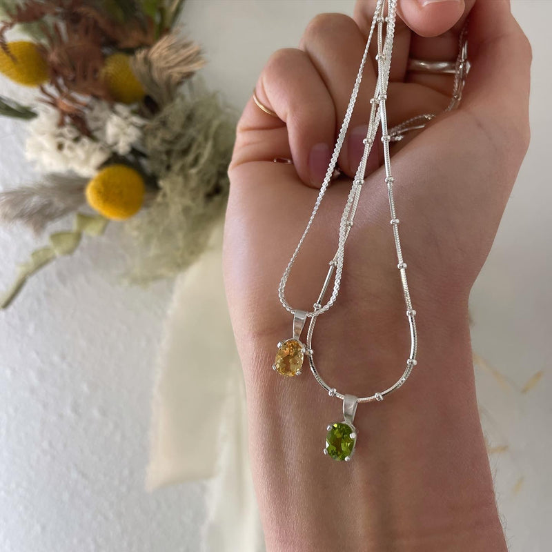 An oval faceted peridot necklace with a silver chain, showcasing a single green peridot stone in a prong setting.