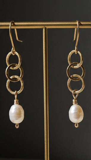 Gold chain earrings with pearl drops on a gold earring stand against a gray background.