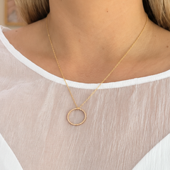 A close-up of a woman wearing a delicate gold necklace with a minimalist circular pendant, styled over a white and sheer puff-sleeve top.