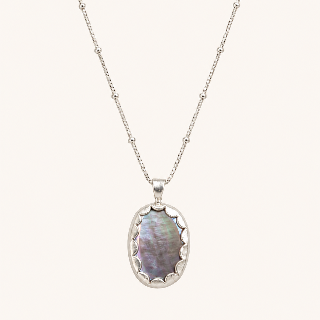 A silver beaded chain necklace with an oval pendant featuring iridescent mother-of-pearl inlay, shown against a solid off-white background.