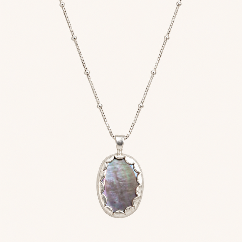 A silver beaded chain necklace with an oval pendant featuring iridescent mother-of-pearl inlay, shown against a solid off-white background.