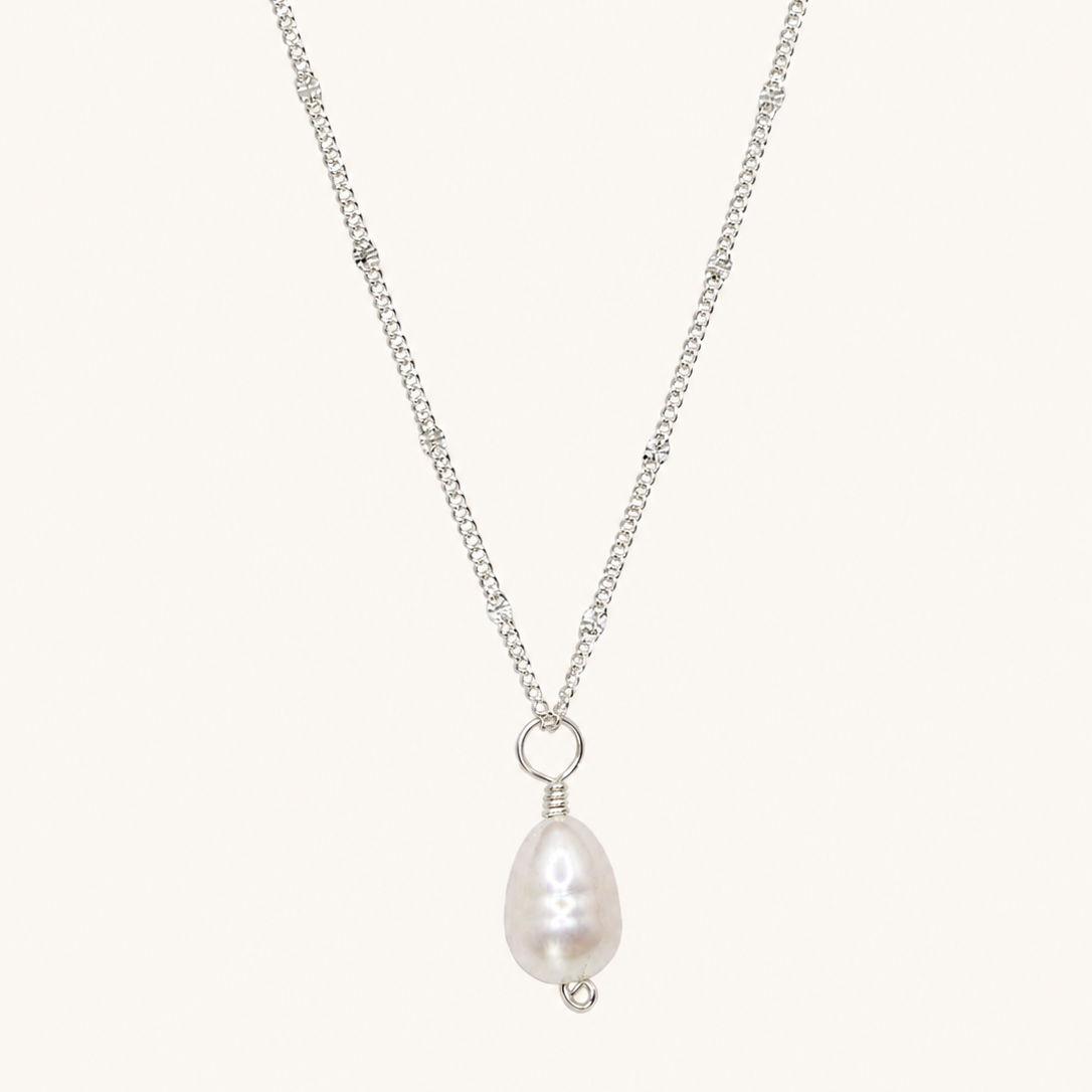 A silver chain necklace featuring a teardrop-shaped white pearl pendant with a small silver bead accent, displayed against a solid off-white background.
