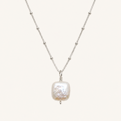 A silver beaded chain necklace featuring a large, irregularly shaped white baroque pearl pendant, displayed against a solid off-white background.