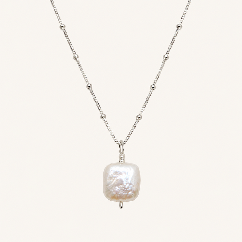 A silver beaded chain necklace featuring a large, irregularly shaped white baroque pearl pendant, displayed against a solid off-white background.