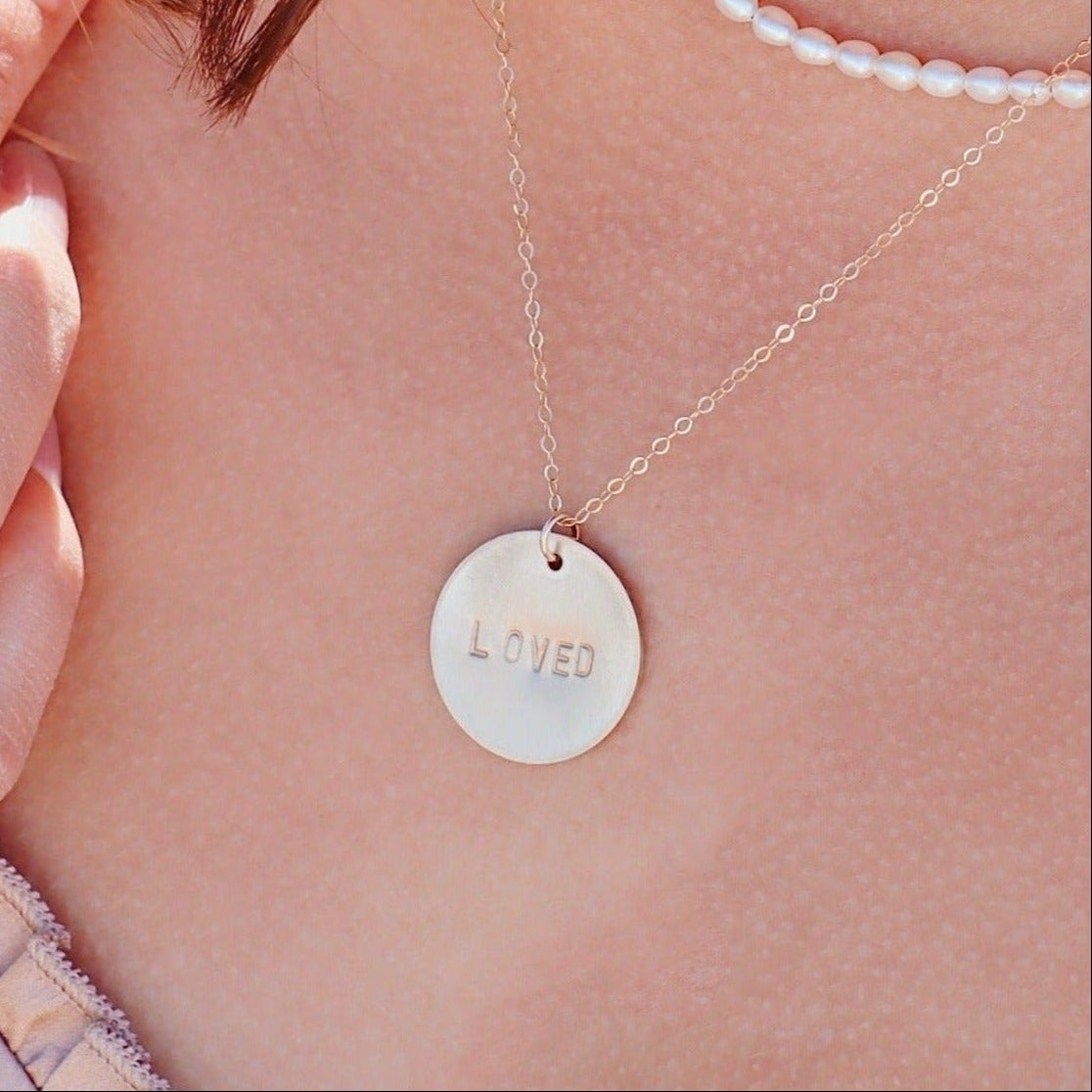 Necklace with a round pendant engraved 'LOVED' on a person's neck.