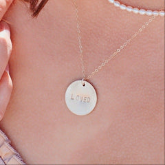 Necklace with a round pendant engraved 'LOVED' on a person's neck.